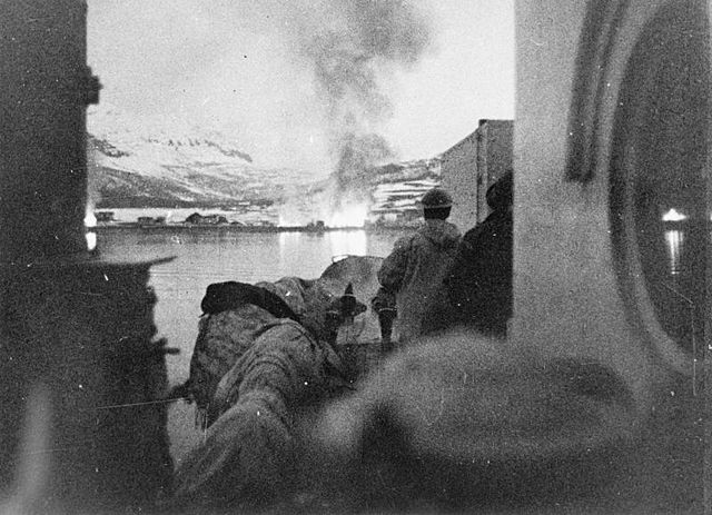 Sort-hvitt foto fra en båt i vinterlandskap. En eksplosjon skimtes mot land.