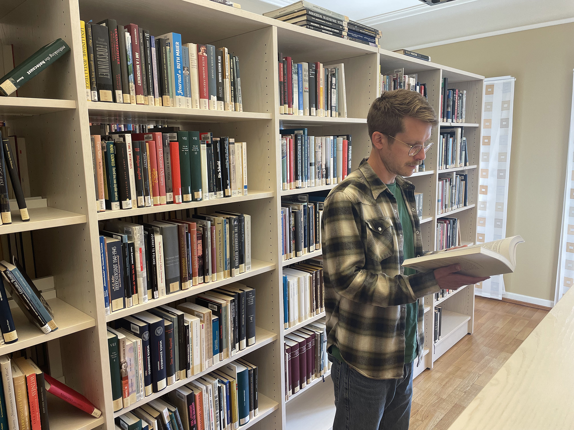 Young man readig a book in front of some book shelfs