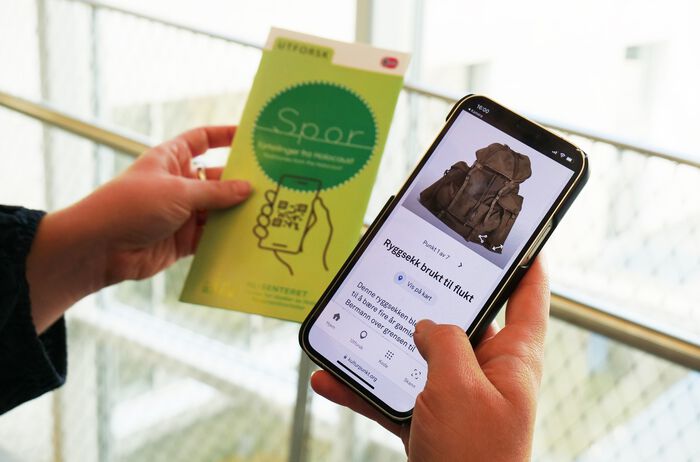 Nærbilde av en mobiltelefon som viser en grønn sirkel med teksten "Spor, fortellinger fra Holocaust"